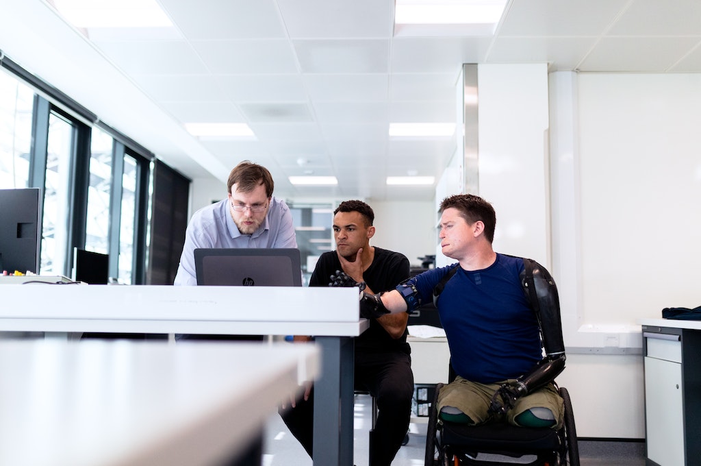 Tres persones, una en cadira de rodes, treballant a una oficina