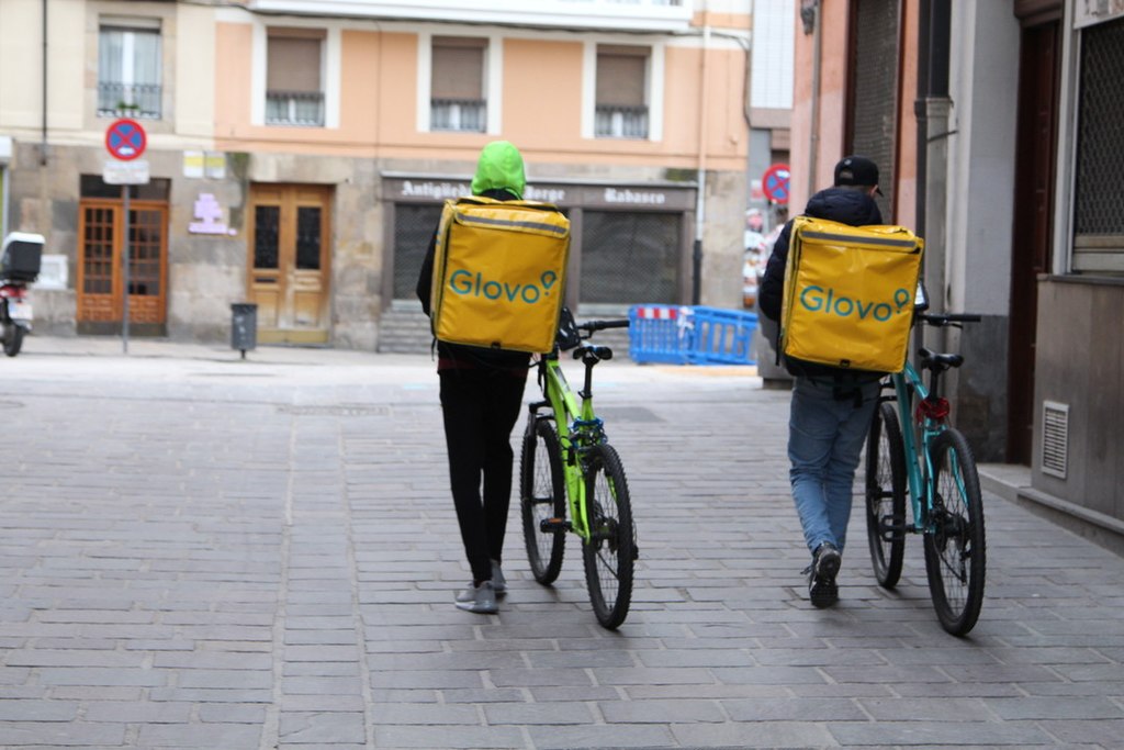 Dos repartidors 'riders' de Glovo caminant pel carrer